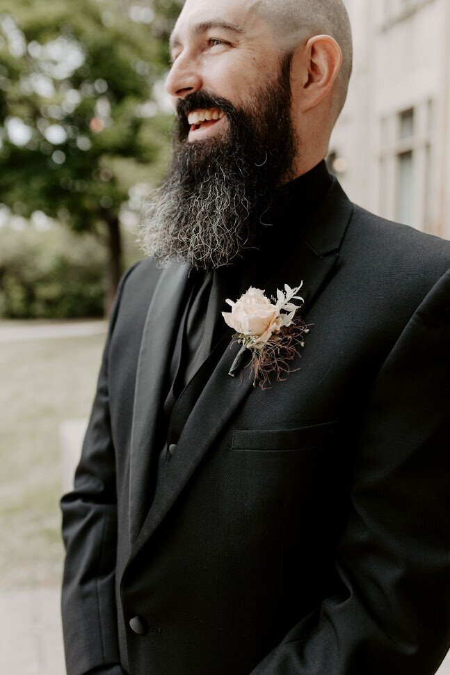 This close-up features the groom beaming in his stylish all-black suit, showcasing a modern taupe boutonniere that adds an edgy touch to his look. The image captures his confidence and joy on this special day, perfect for couples in Ottawa looking for unique wedding inspiration and ideas for groom’s attire.