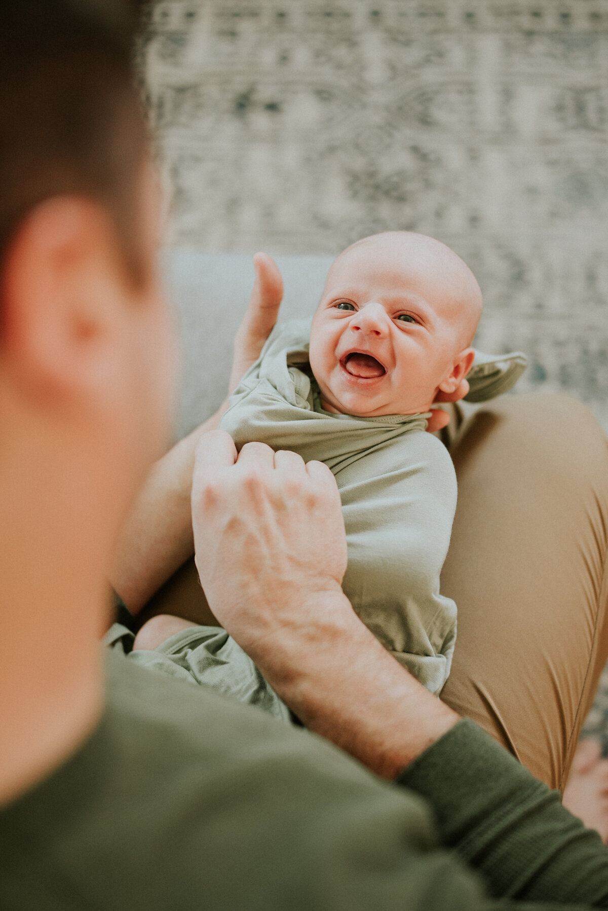 In the heart of Champlin, this heartwarming image captures a precious newborn baby boy as he shares a beautiful moment with his dad. Lay back on his lap and adorned with a joyful smile, this little one undergoes a clothing change, creating a memory of the loving bond between father and son.