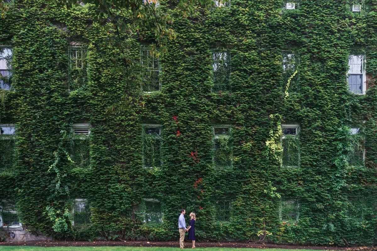 Couple standing small against a massive ivy-covered building