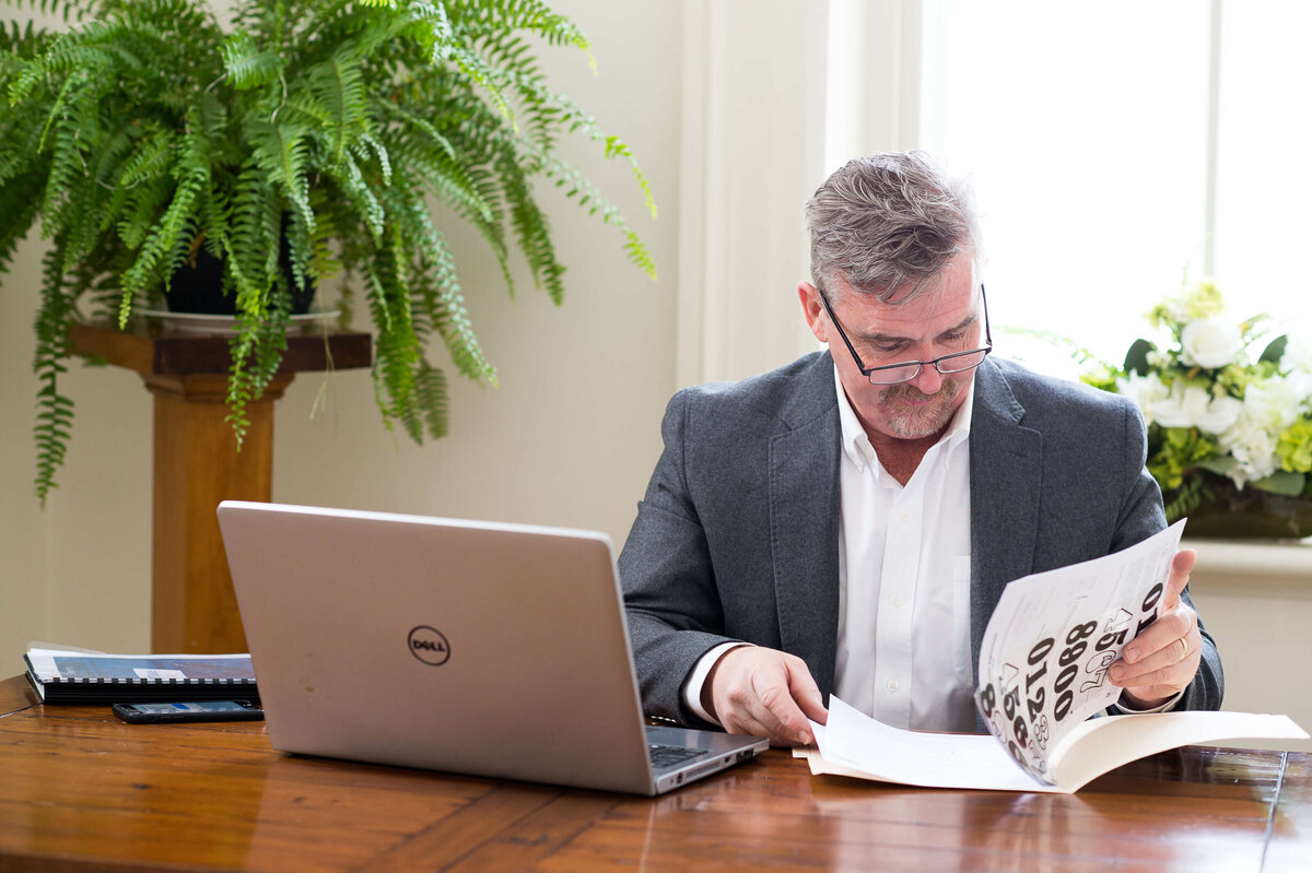 a photo of a male realtor sitting at his desk flipping through housing documents for clients.  Captured on location by Ottawa Branding Photographer JEMMAN Photography COMMERCIAL