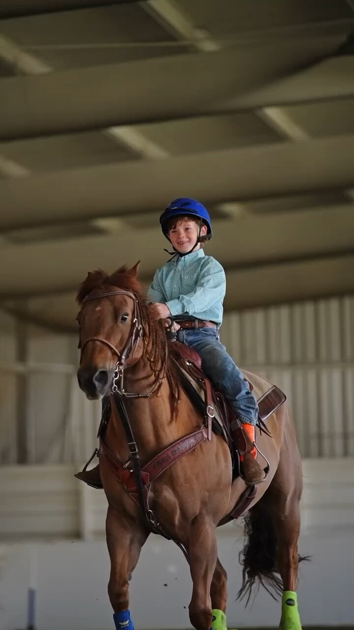 A young rider is cantering on a chestnut pony, he is riding in a western saddle, he is smiling 