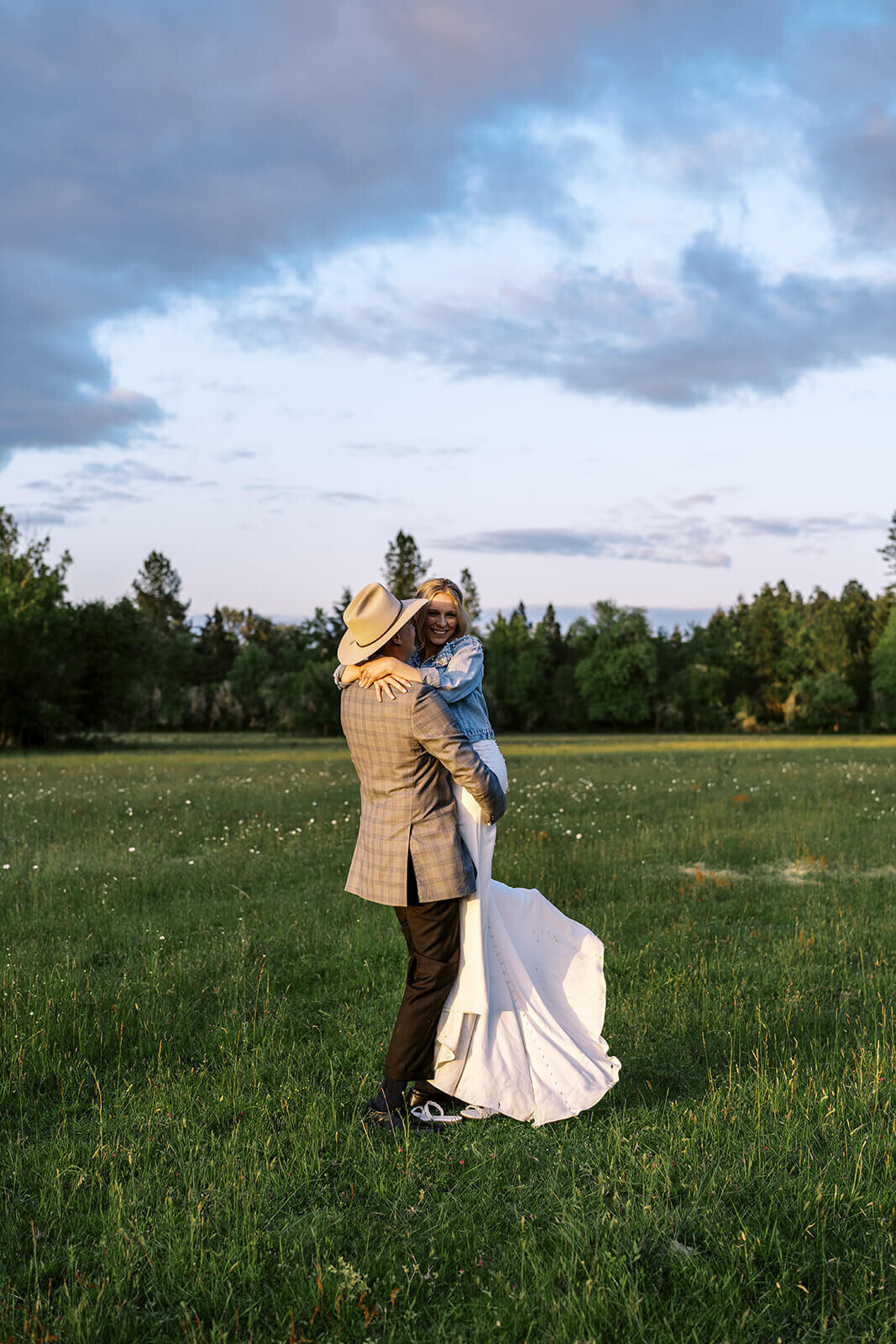 A groom lifts his bride in a green field.