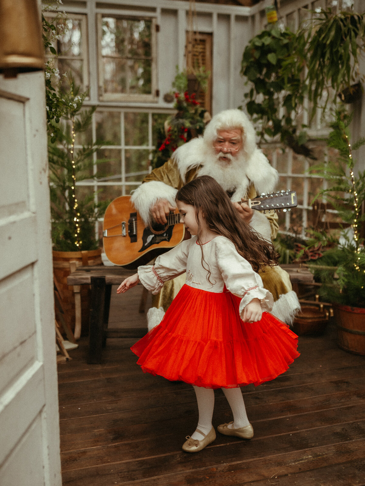 A little girl wearing a bright red skirt dances while Santa plays guitar at Das Hinterhaus.