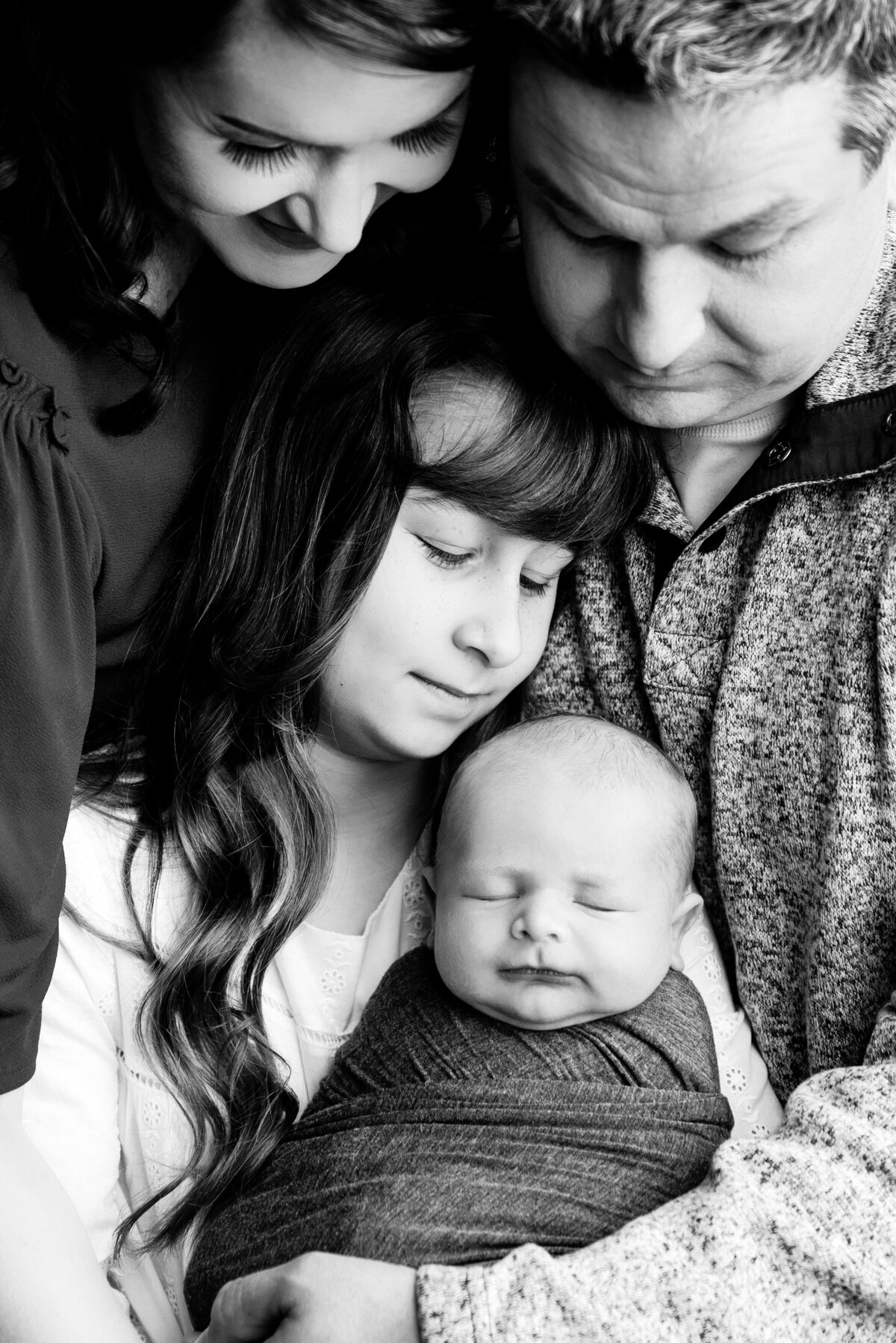 st-louis-newborn-photographer-blac-and-white-photo-of-baby-swaddled-and-held-by-older-sister-mother-and-father