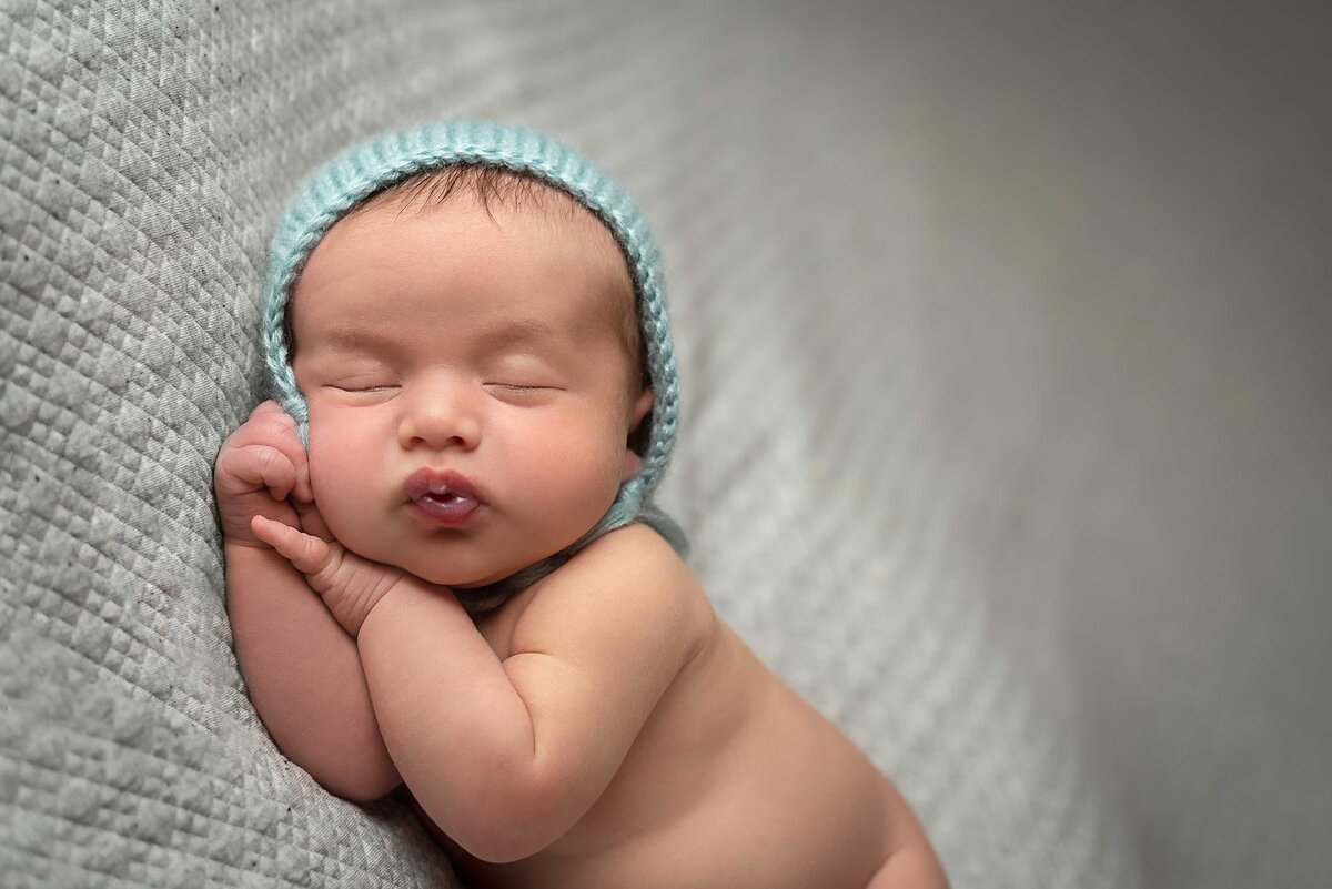 Newborn baby boy wearing only a blue bonnet with his  lips puckered.