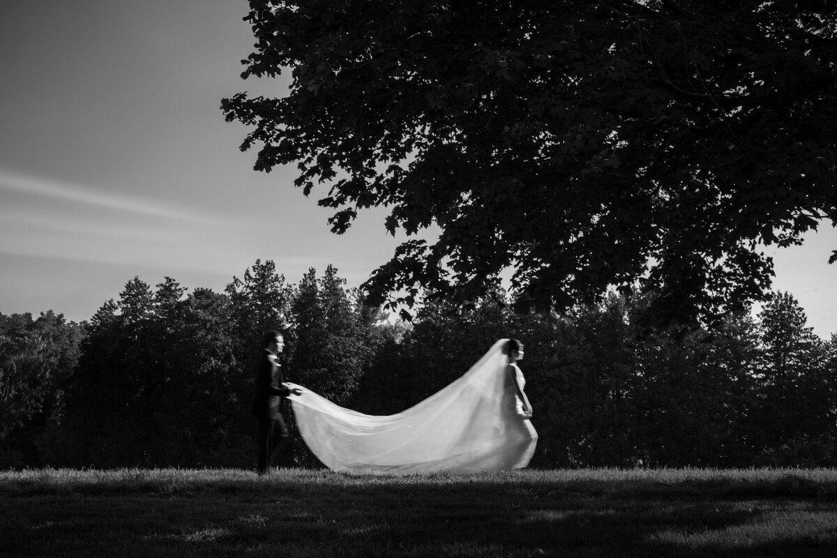A bride and groom walk across a field at a destination wedding in Vermont