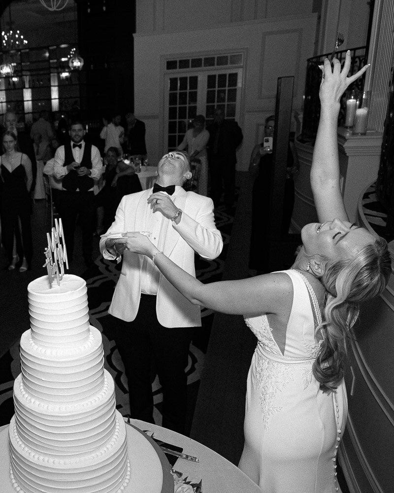 bride and groom throw their arms up in the air after cutting their wedding cake during their reception at Cescaphe Ballroom