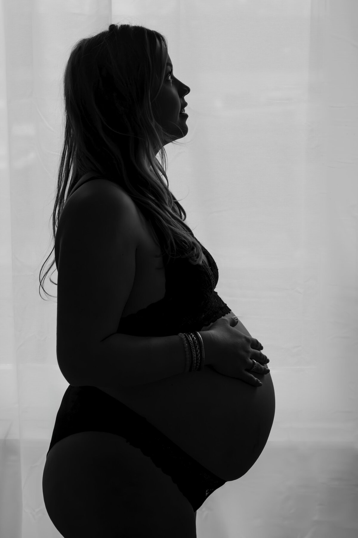Zwart-wit afbeelding van een zwangere vrouw, die haar buik liefdevol aanraakt met een serene uitstraling.