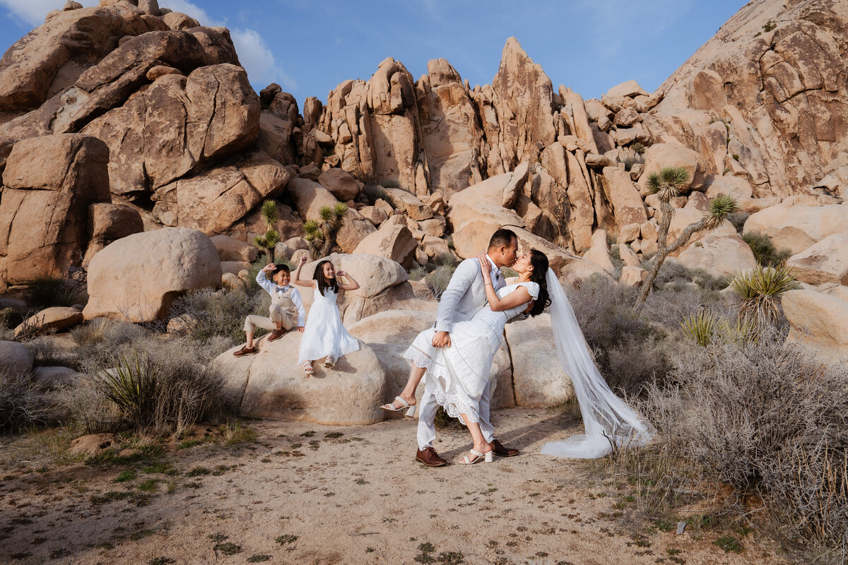 Joshua Tree elopement with bride and groom at Hidden Valley doing a dip and kiss in front of their kids.