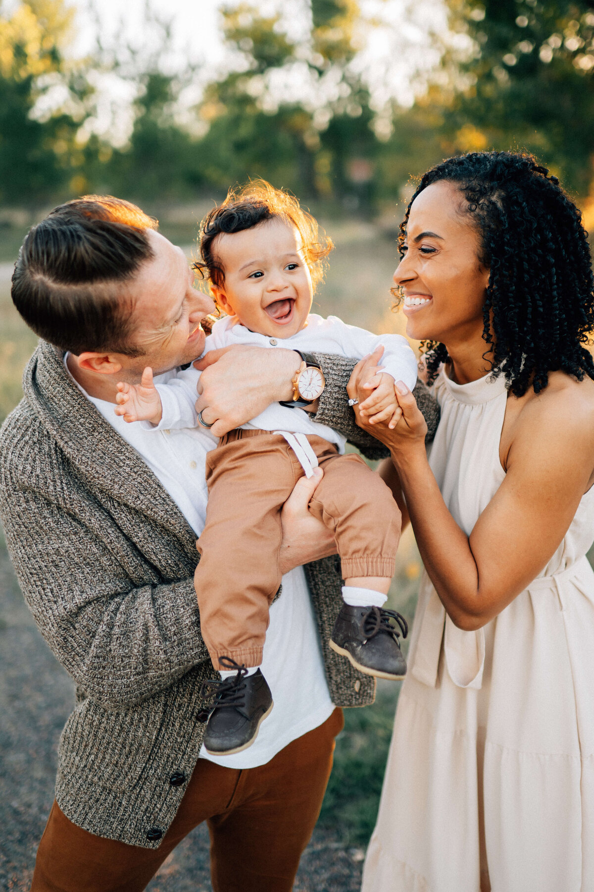 family of three in the sunset with mom and dad holding giggling baby