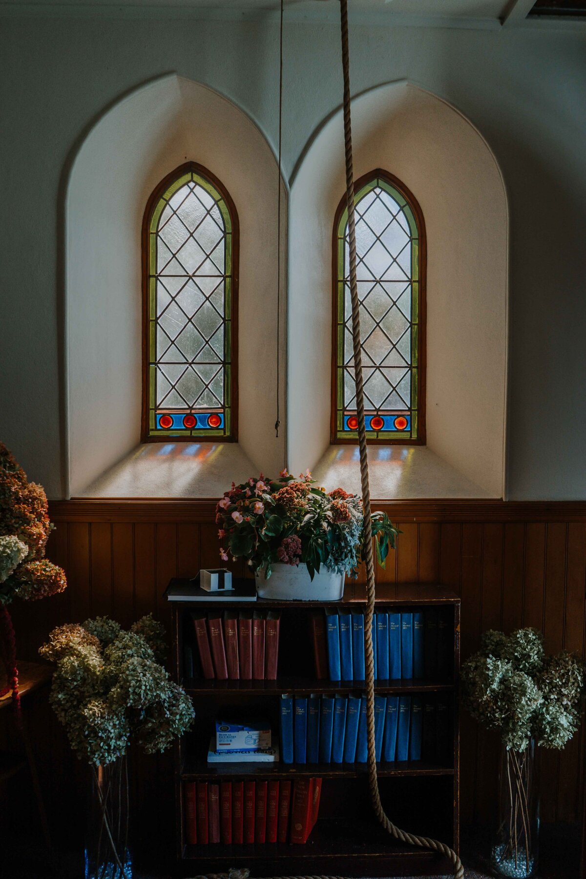 stained glass windows inside of a church with bell rope and flowers