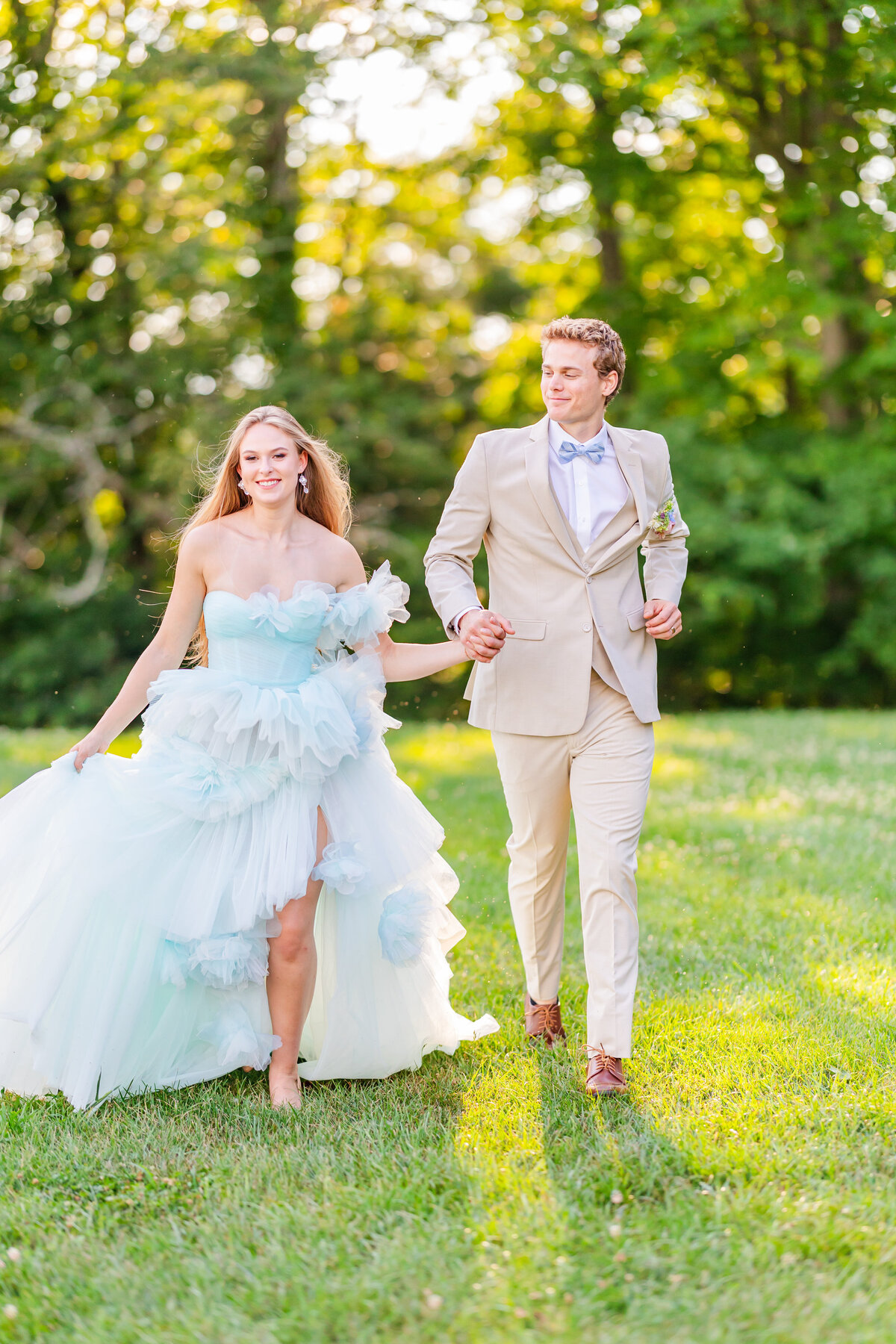 groom in brown suite with bow tie and bride with blue chiffon dress running holding hands