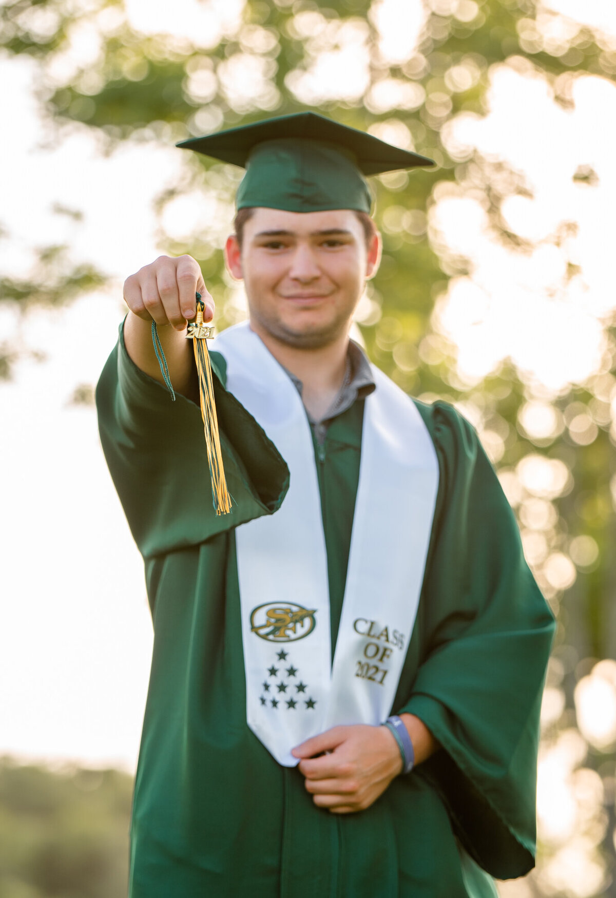A Santa Fe senior wears his cap and gown while holding his tassel towards the camera.