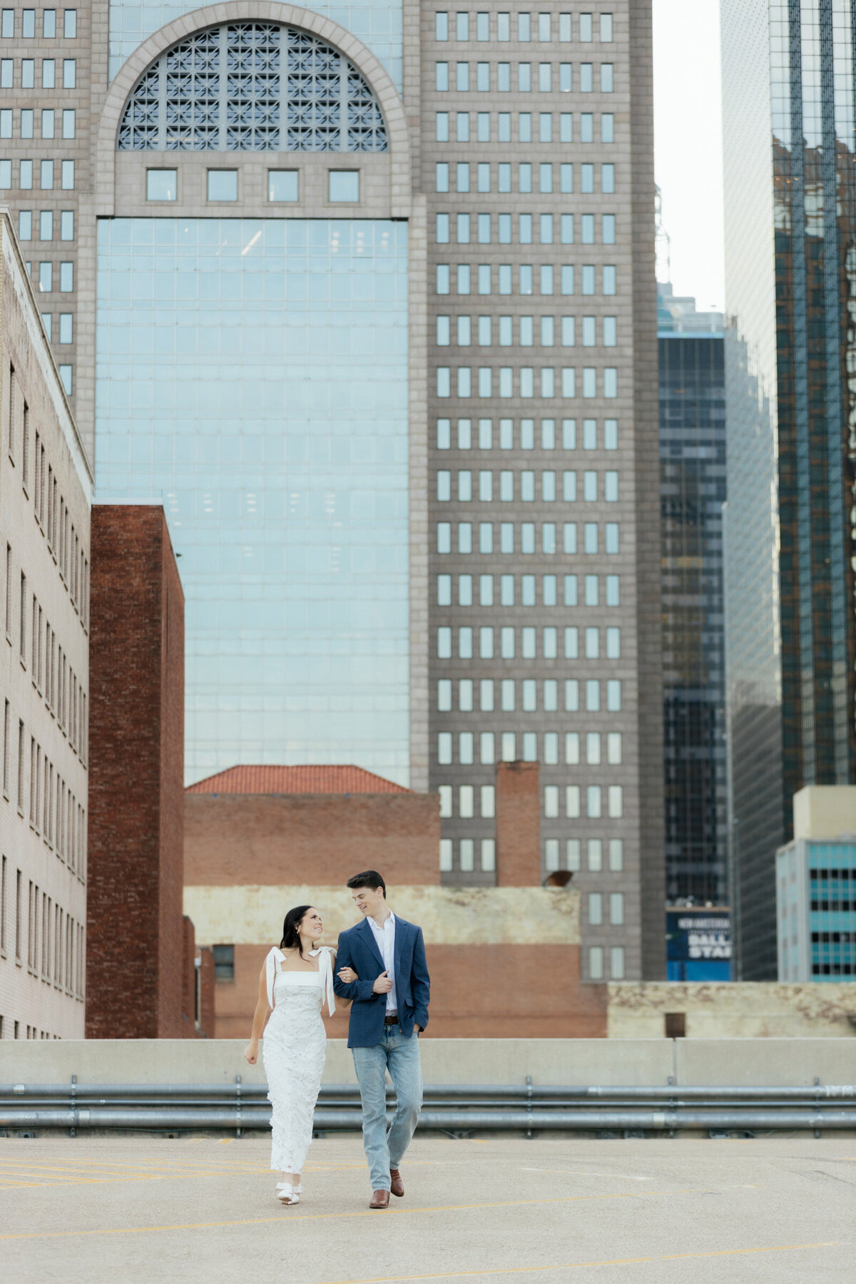 Couple walking with the Dallas skyline behind them during their engagement session.