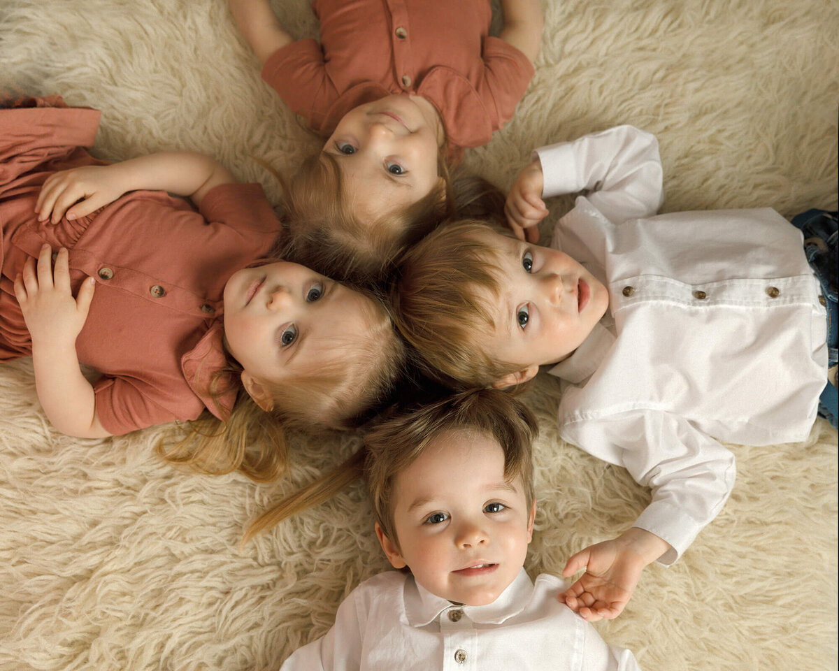 Quadruplets all laying on a white creme rug looking up.