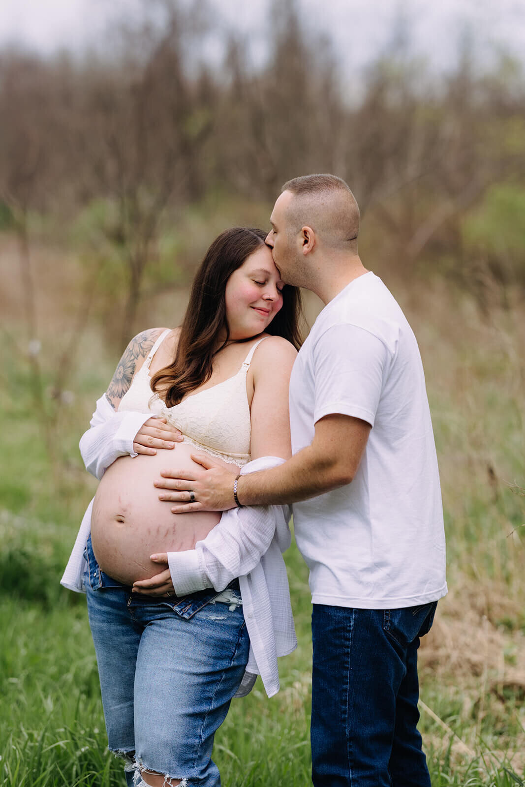 Man rests hand on womans baby bump in grass area at  Finger Lakes Maternity session