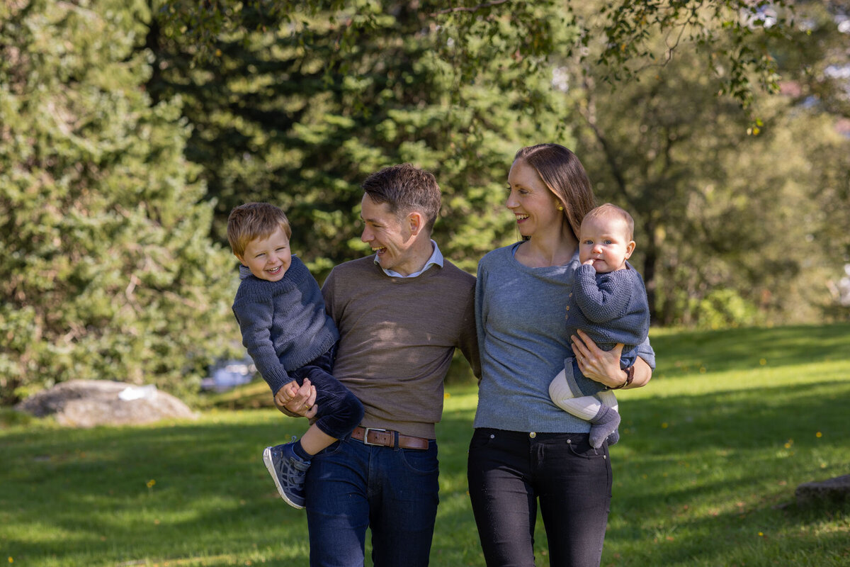 Famileportrett der familien går mot fotografen -far bærer storebror, mor bærer lillebror.Fotografert i Langhaugparken av Fotograf Linn Landmark.