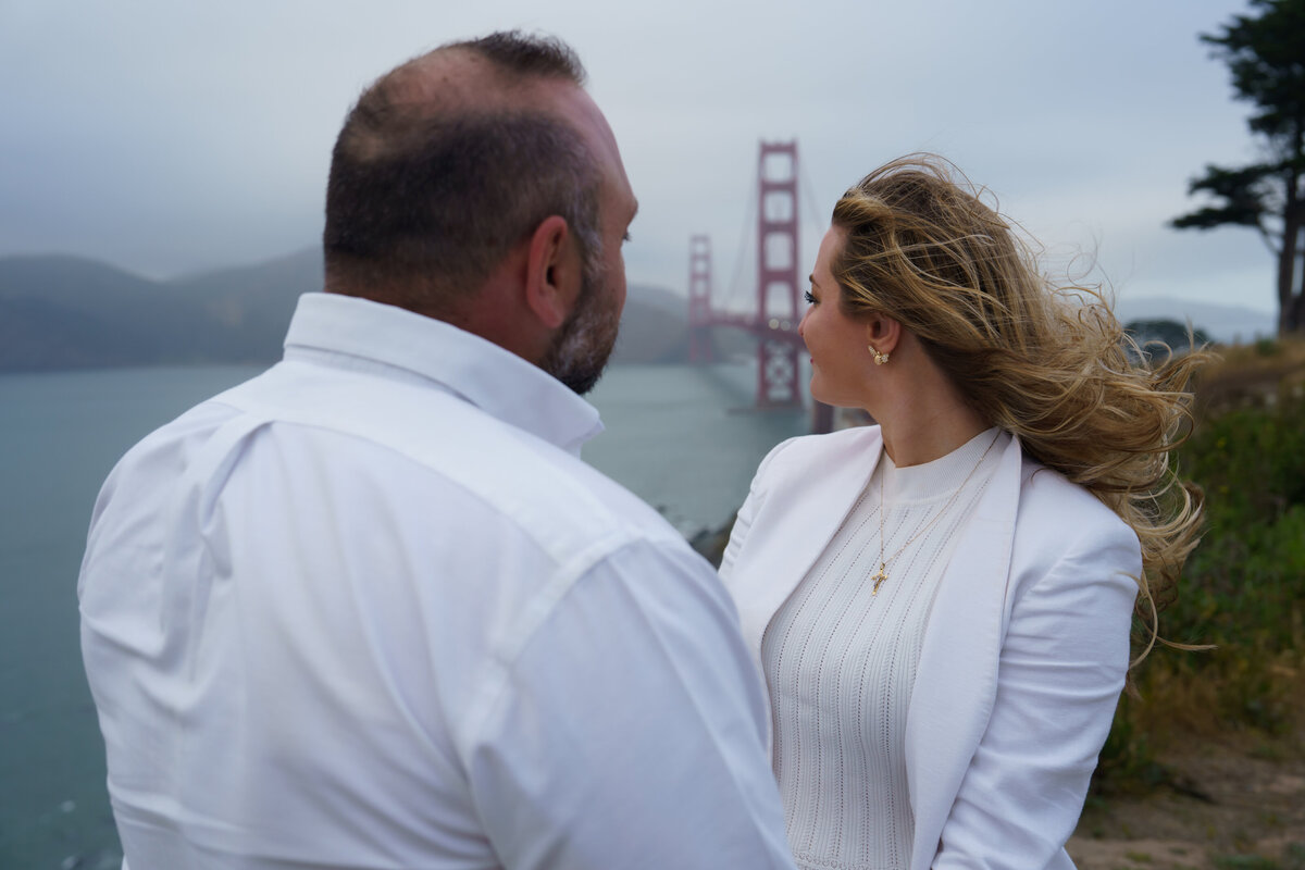 Couple holding hands looking back at the golden gate bridge near sunset