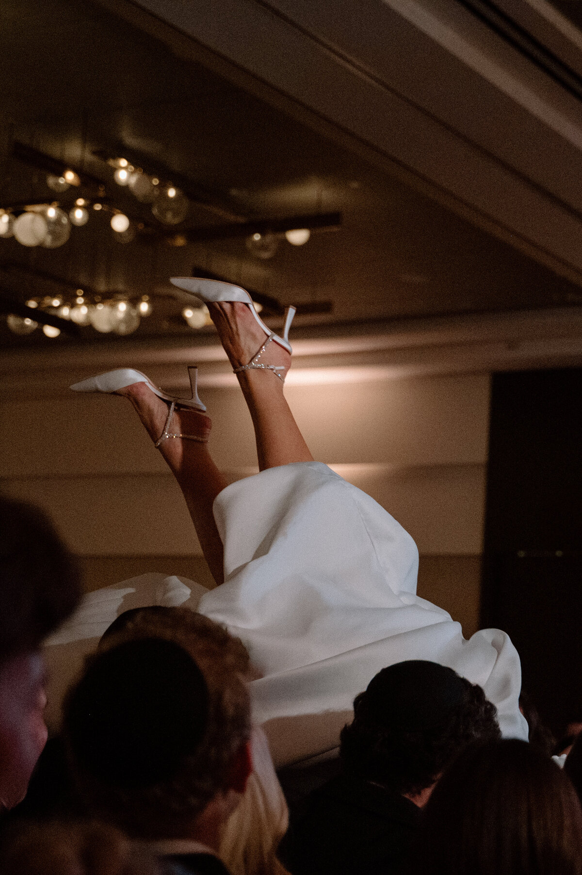 Close-up of bride’s legs and heels in the air during energetic hora dance.