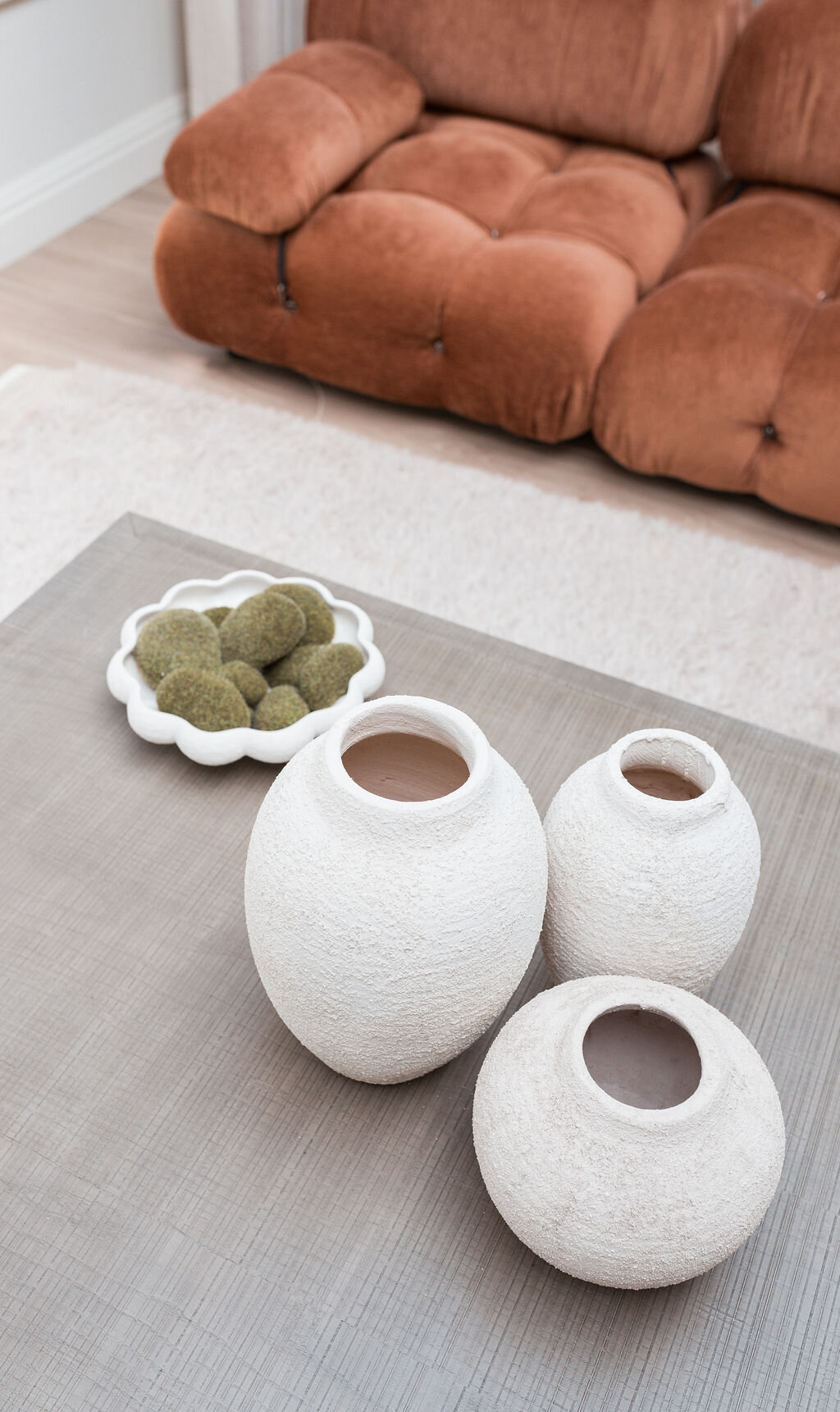 Details of the textured white vases on the wooden coffee table in a cozy living room.