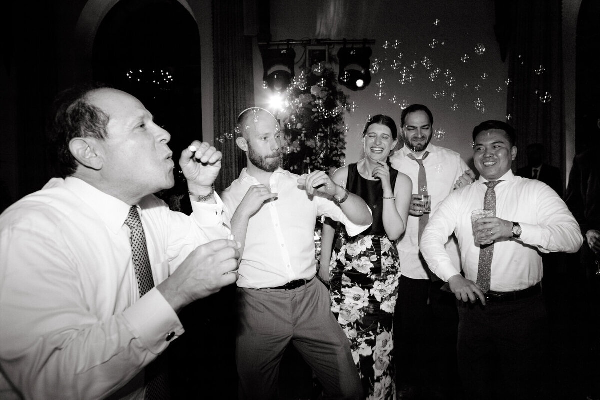 A black and white photo of a woman and four men, wearing formal attire, laughing while dancing