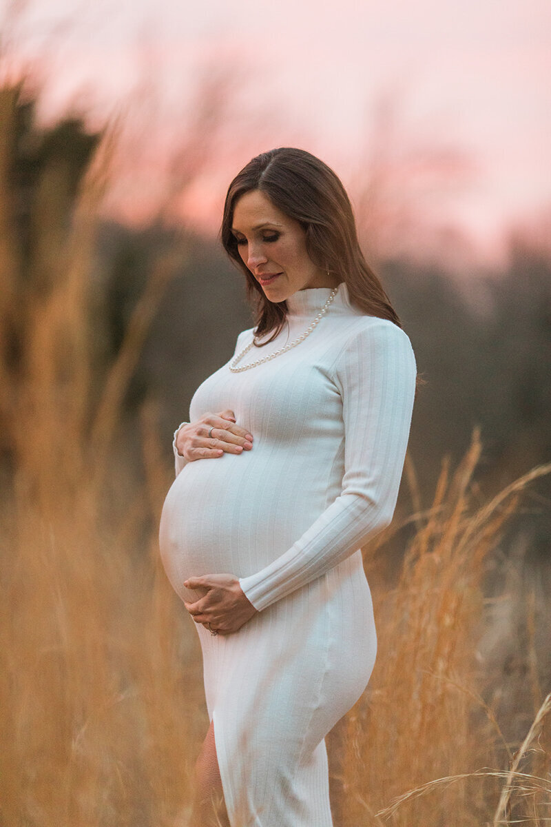 pink sunset sky and tall golden grass surround a pregnant mom as she poses for her maternity photos