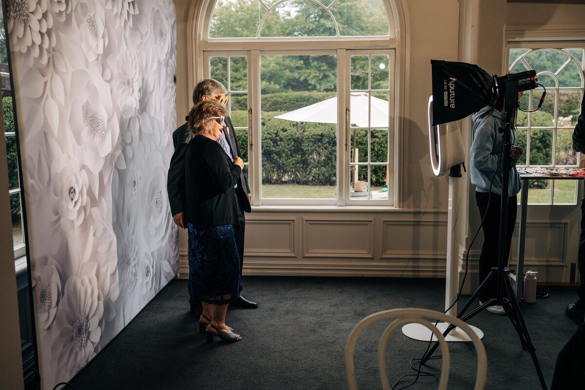 a white freestanding photo booth with white paper flowers backdrop set up at pemberton wedding venue in christchurch with windows and trees beside it