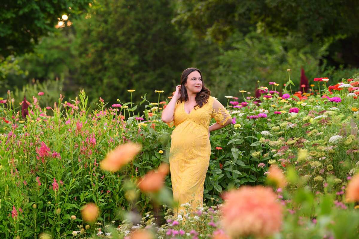 pregnant woman wearing a yellow maternity dress in a flower field for her Burlington, Ontario maternity photography session
