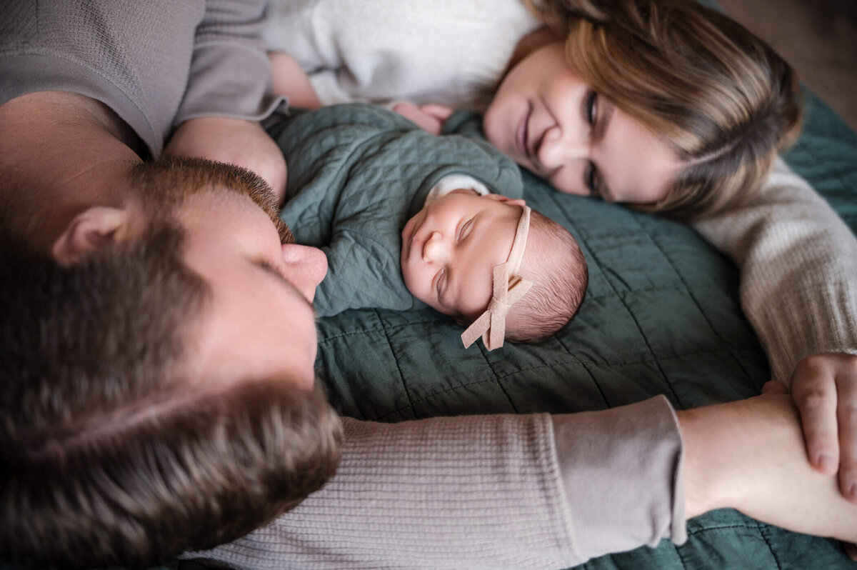 Husband and wife laying on a bed with their newborn in between them getting newborn photos taken