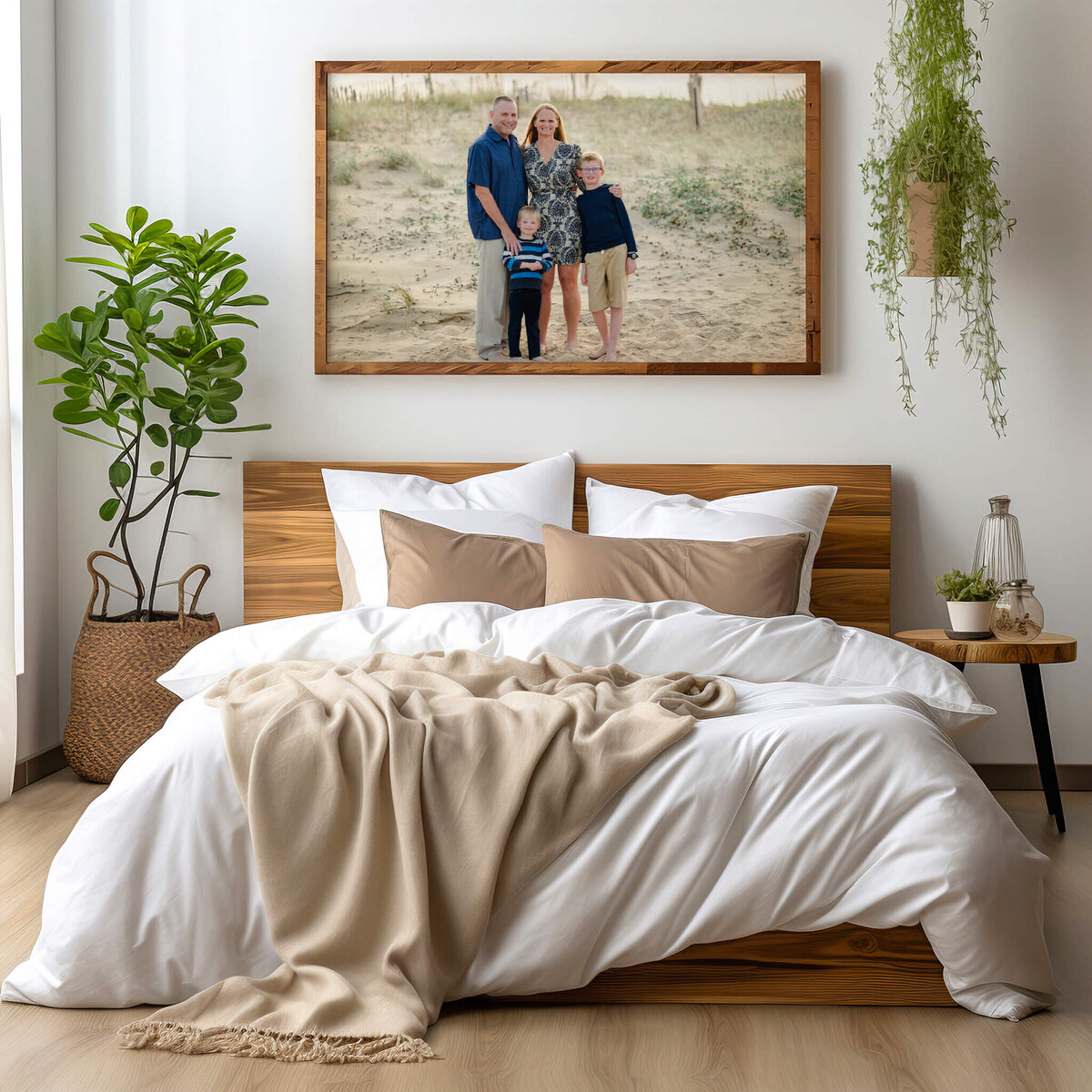 A family of four, all wearing blue, are pictured at the beach. The picture is framed and hanging above a bed made in white with brown accents.