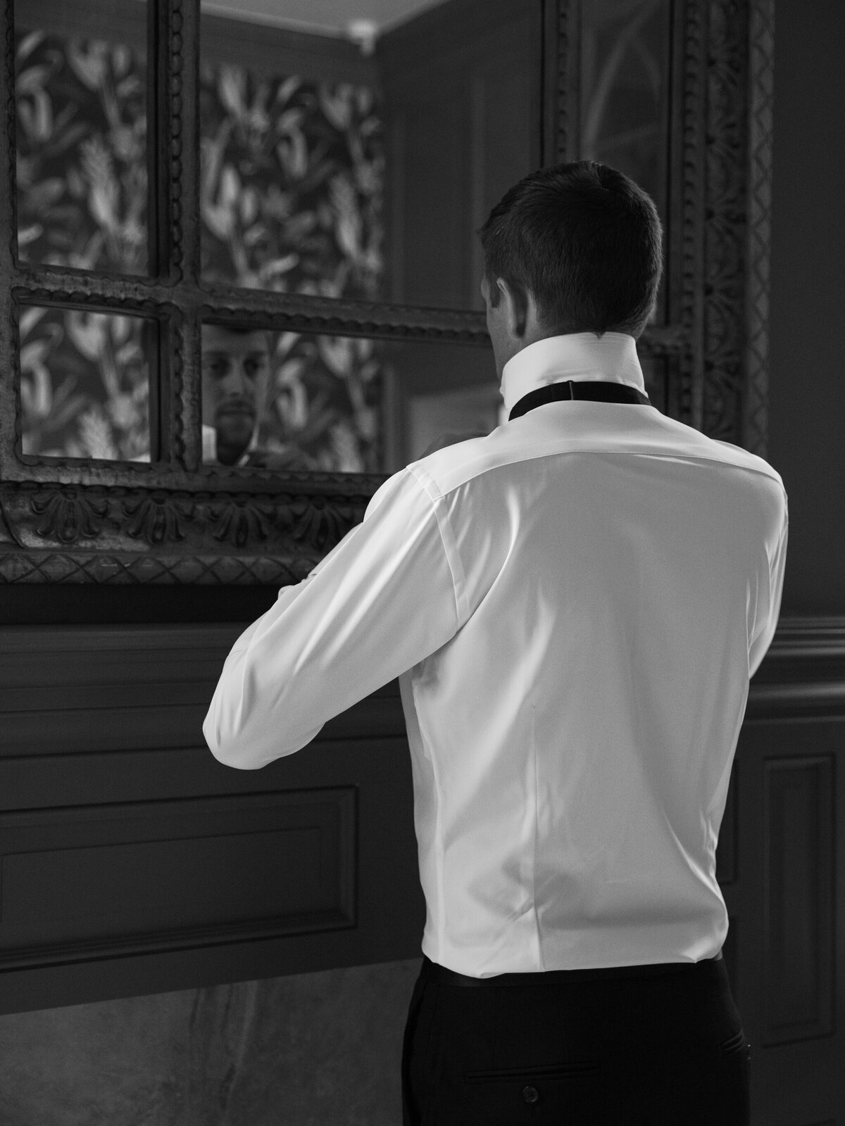 Rust Manor House Wedding | A black and white image of groom tying his tie in a mirror 