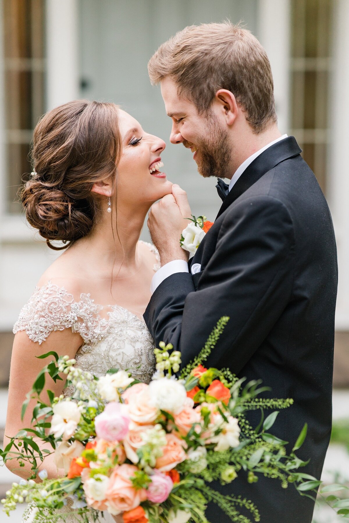A bride and groom smile and laugh as they lean in for a kiss in front of Holt House wedding venue in Lexington, NC.