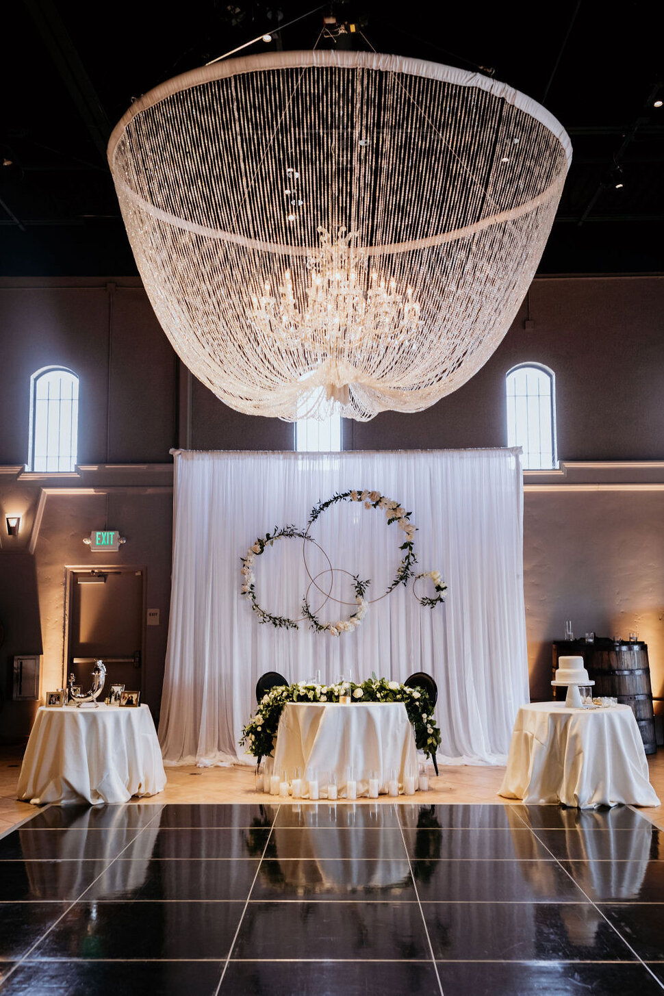 Sweetheart table setup at the Palm Event Center in Pleasanton, CA, for a spring wedding. The elegant arrangement features a stunning chandelier as the centerpiece, with a sophisticated color scheme of gold, black, and white. The table is adorned with refined decor and floral accents, creating a romantic and luxurious atmosphere.