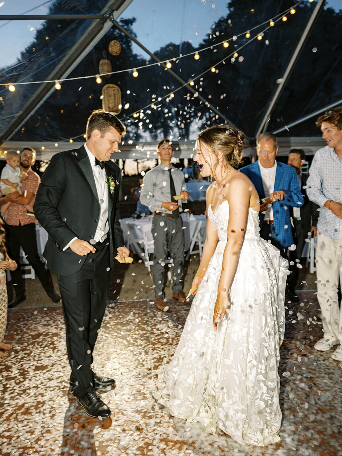 A bride and groom celebrate at night with thrown confetti. 