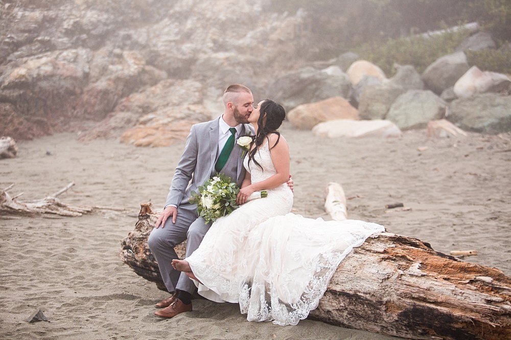 Newly wed couple sitting on driftwood on Oregon Coast