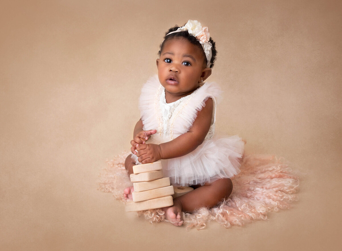 baby girl in lace outfit playing with wooden toy during baby photography nyc session 