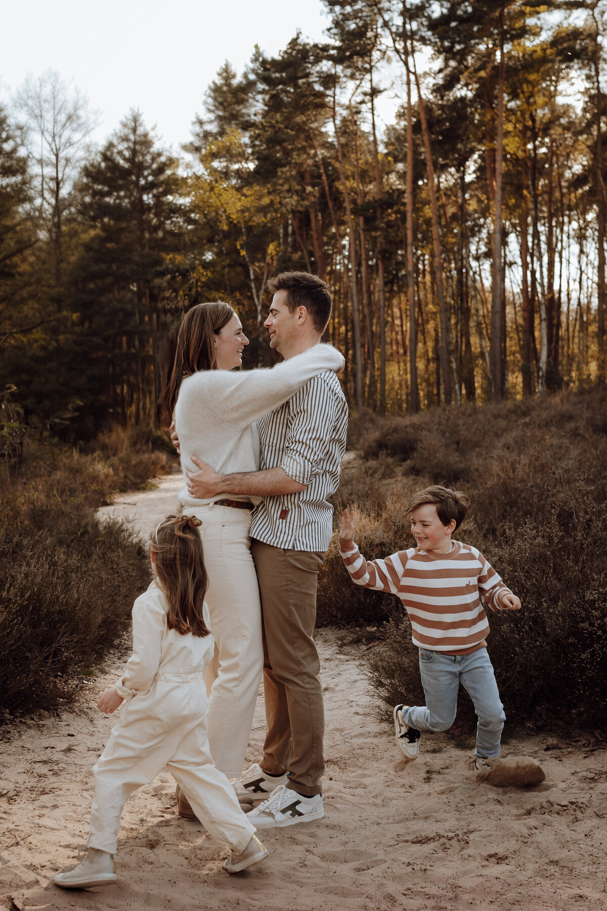 Koppel omhelst elkaar en kindjes spelen er rond tijdens familie fotoshoot in het bos in Antwerpen