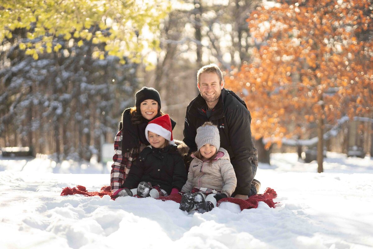 Family of 4 sitting in the snow at Mackenzie King Estate in Gatineau Park