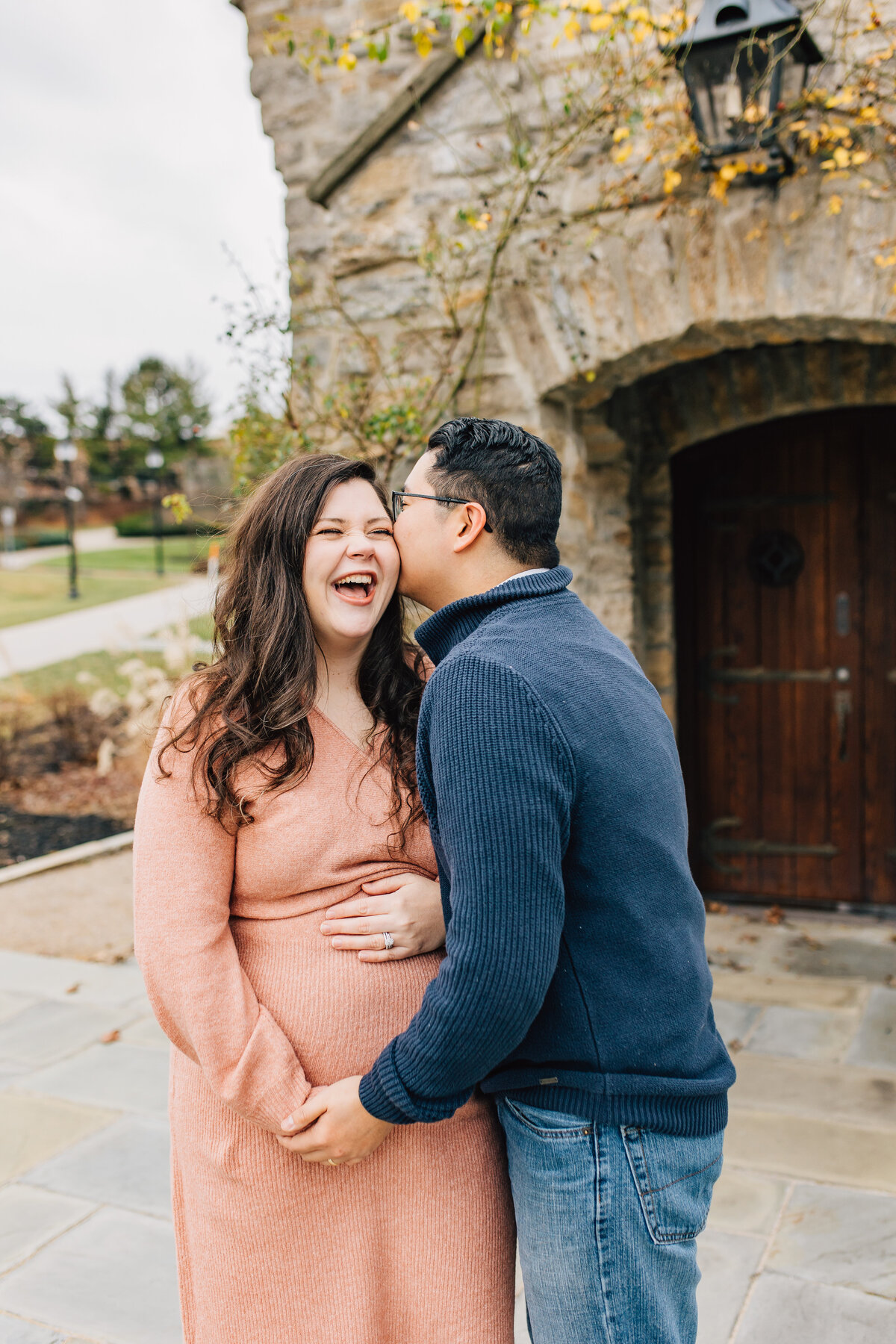 husband kisses pregnant wife on the cheek as she smiles