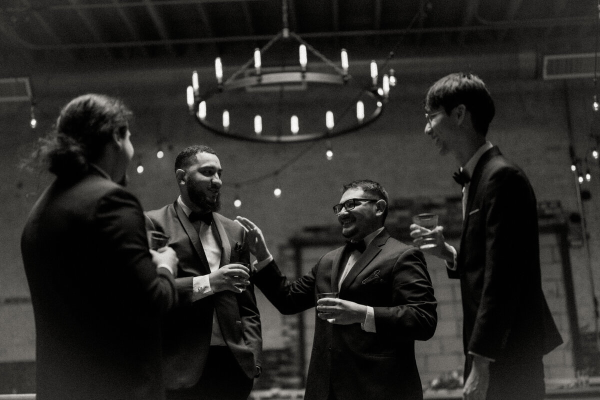 A lively black-and-white scene of the groom with his groomsmen sharing laughter at the Brake and Clutch Warehouse, depicting friendship and joy.