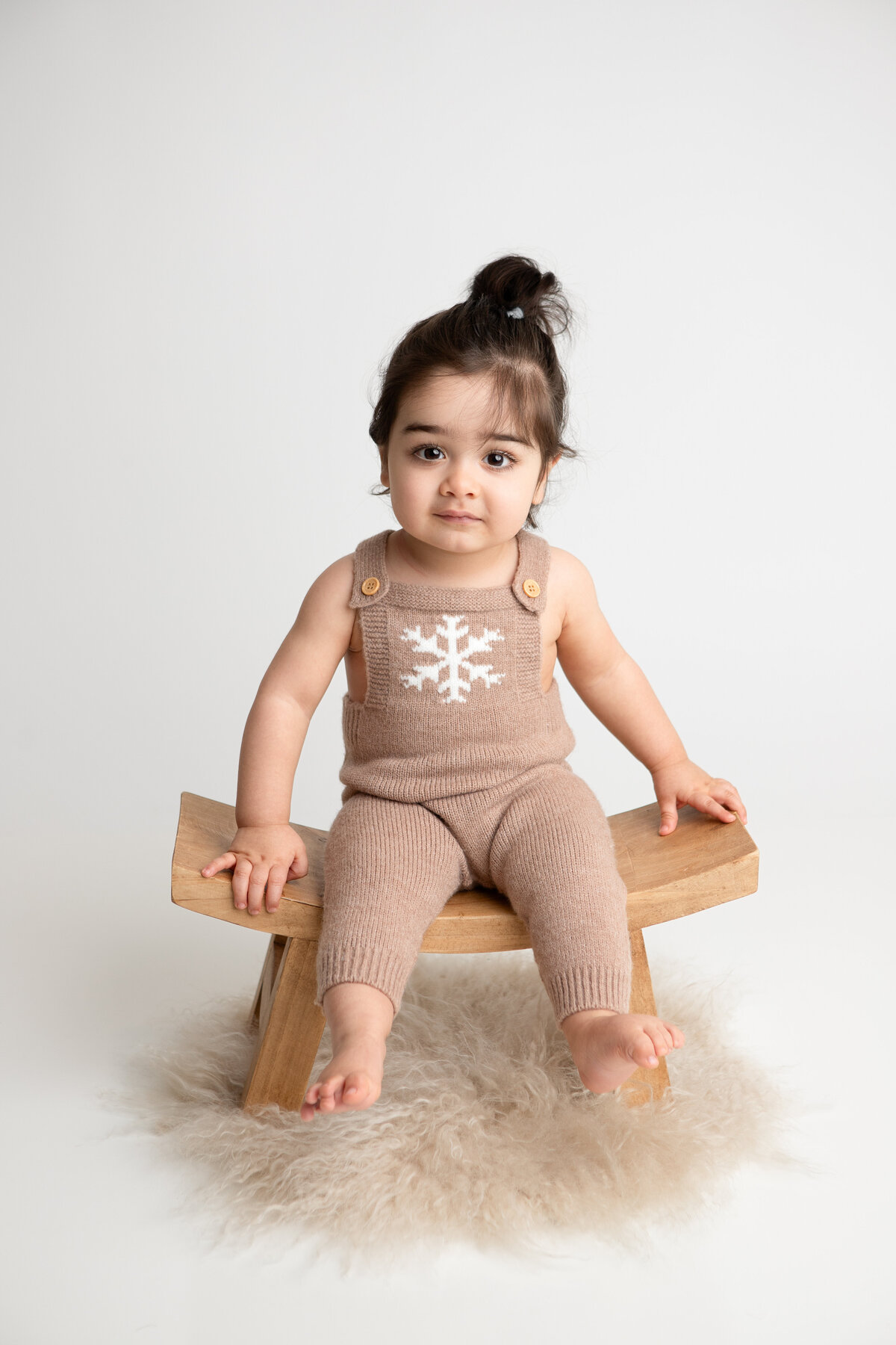 Little boy sitting on a wooden stool with a plain white backdrop