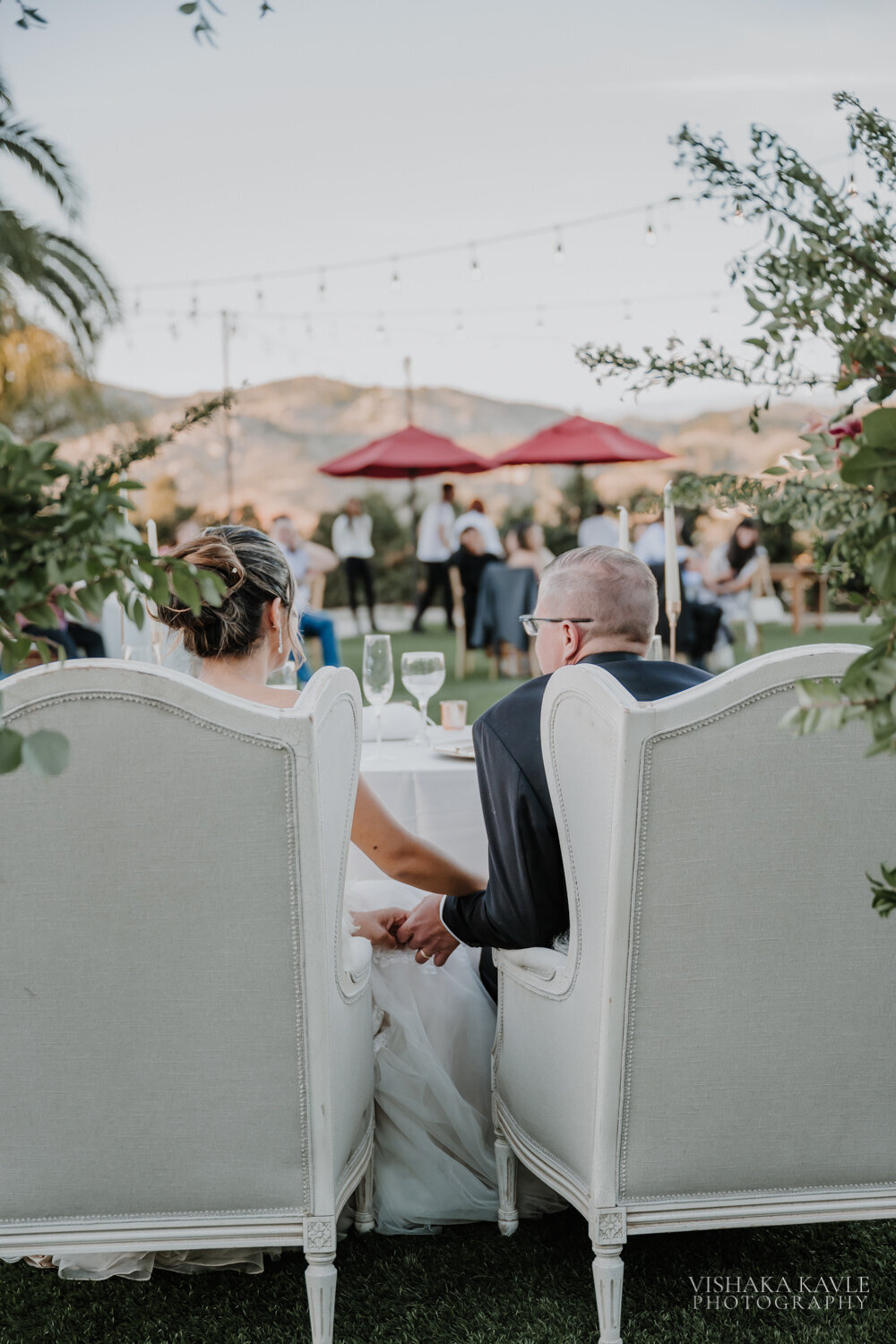 bride and groom sitting in large white chairs while holding hands
