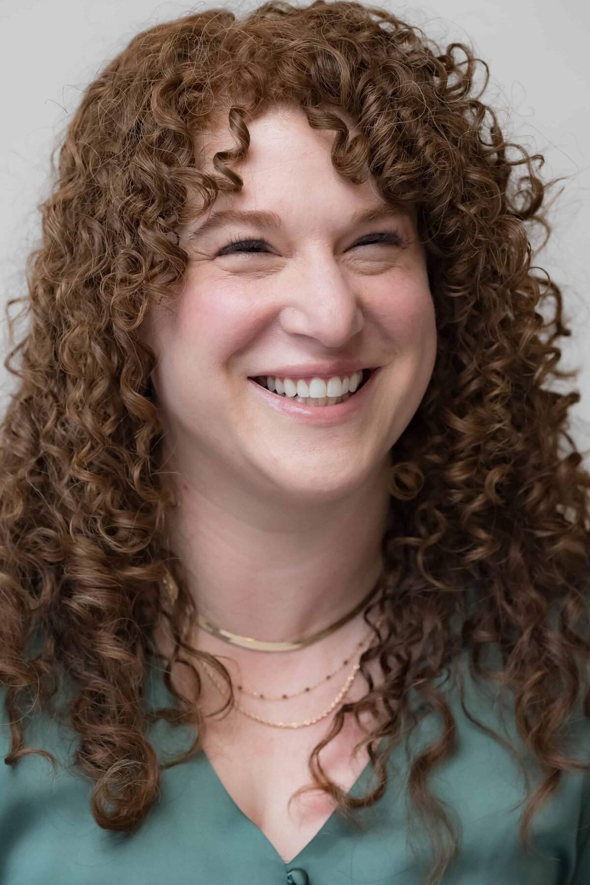 Woman with long red curly hair laughing while posing for a headshot photo