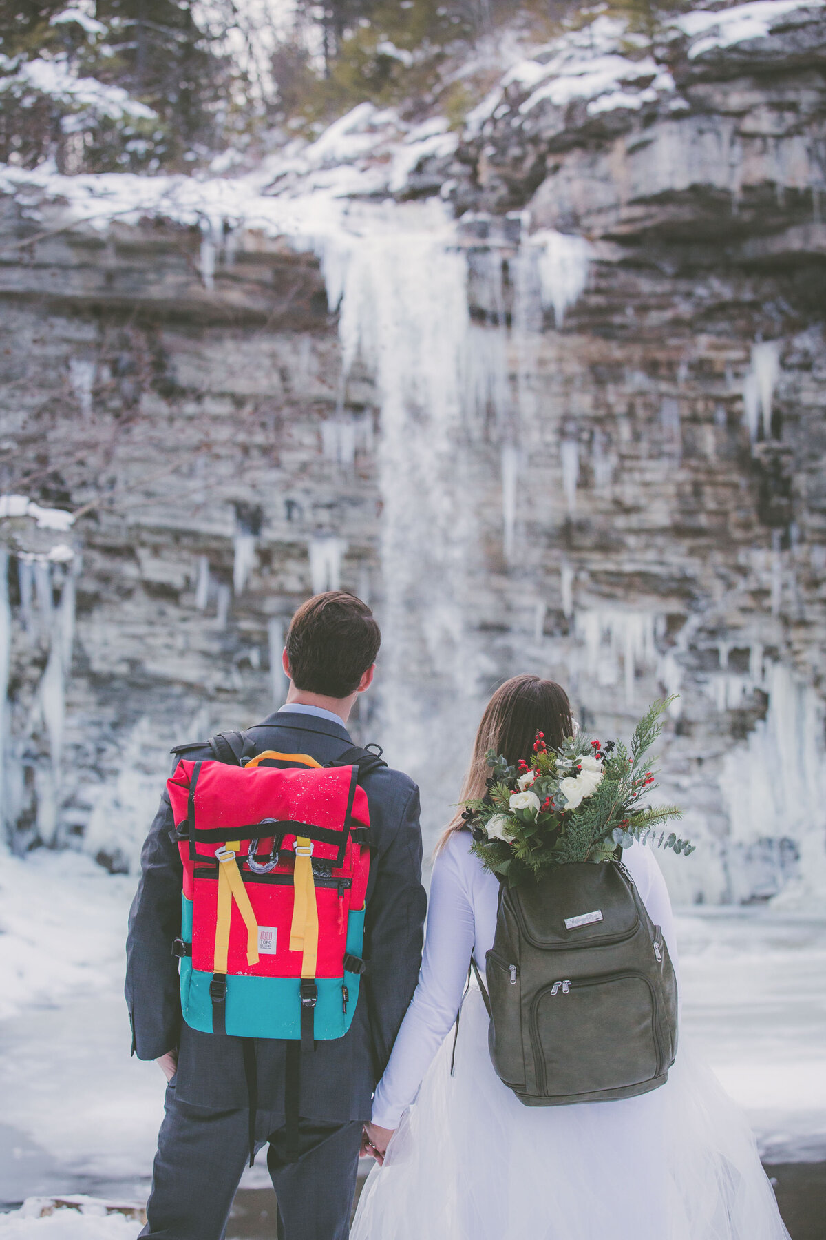 Hiking groom and bride take a moment to look at waterfall during their elopement.