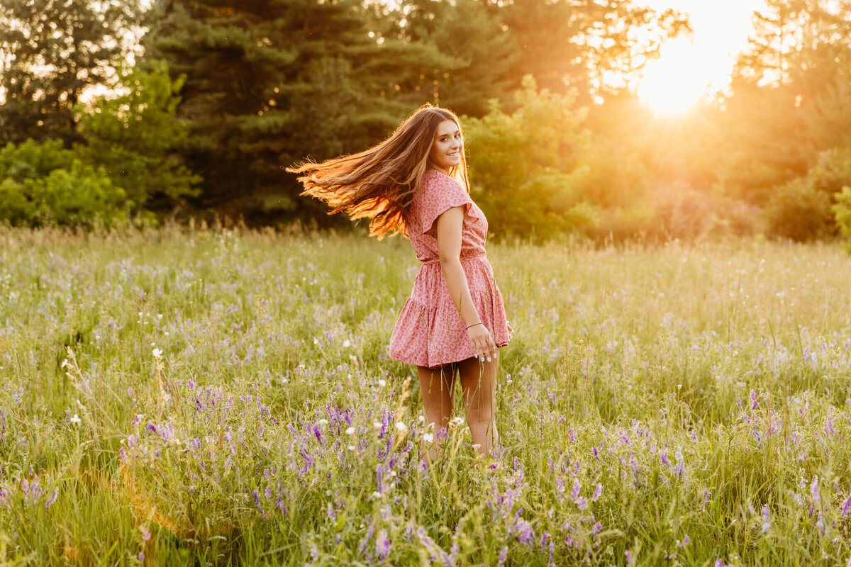 golden hour portrait of a teen girl spinning in a flower field as the sun sets behind her