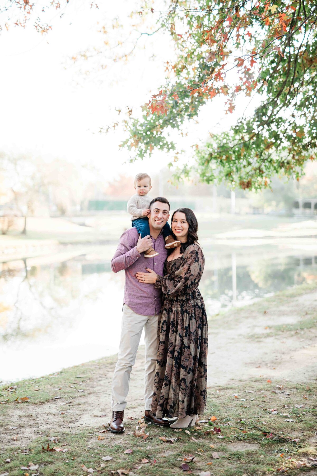 Young parents standing in front of lake with their son on their shoulders