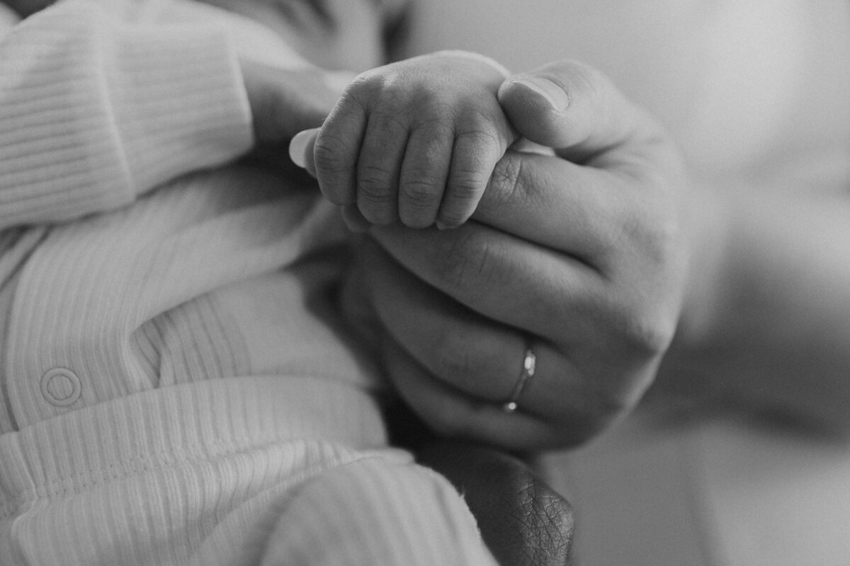 A newborn's tiny hand grasping a parent's finger, a tender and timeless black and white moment in fine art family photography.