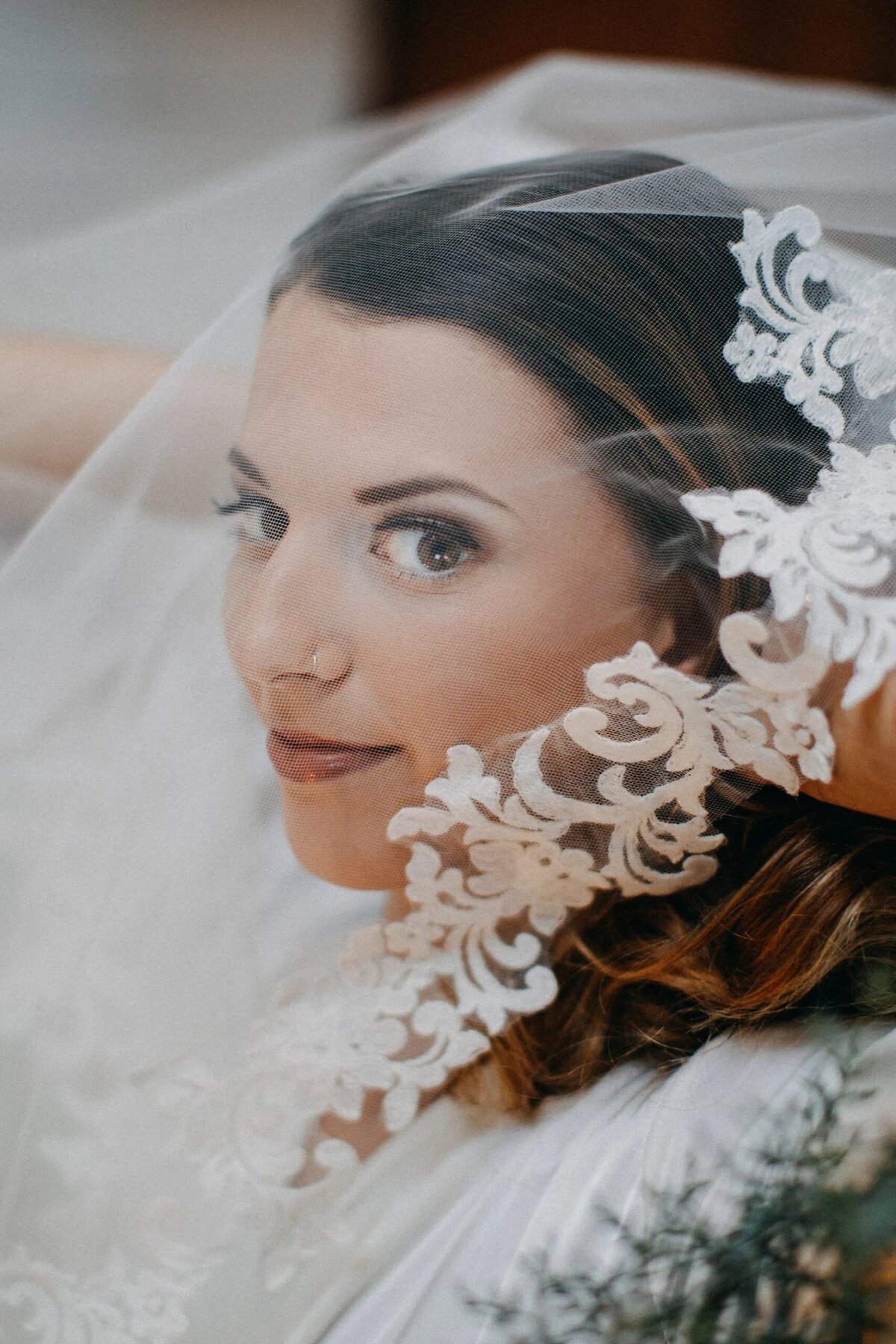 A bride's face is partially veiled by her ornate lace veil