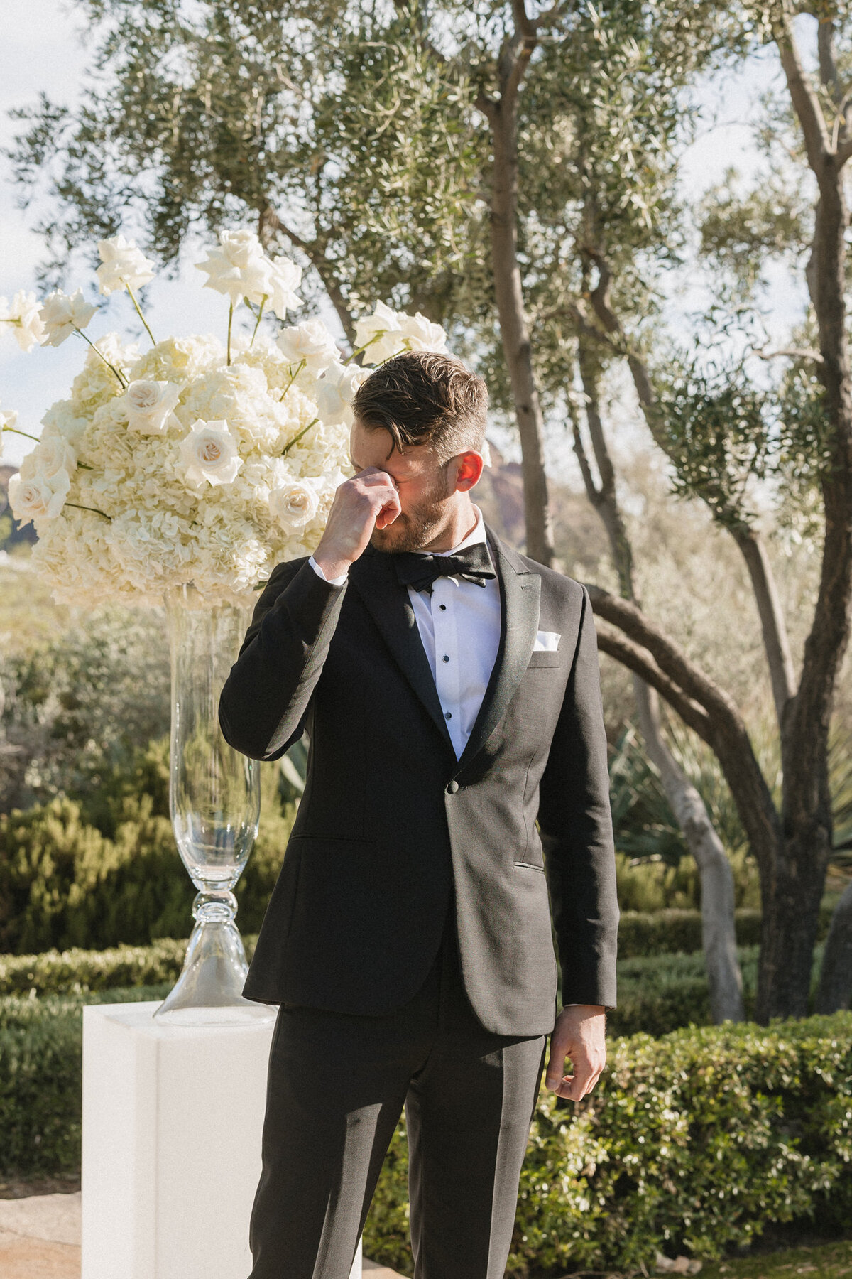Groom wiping tears seeing bride walk down aisle at wedding ceremony