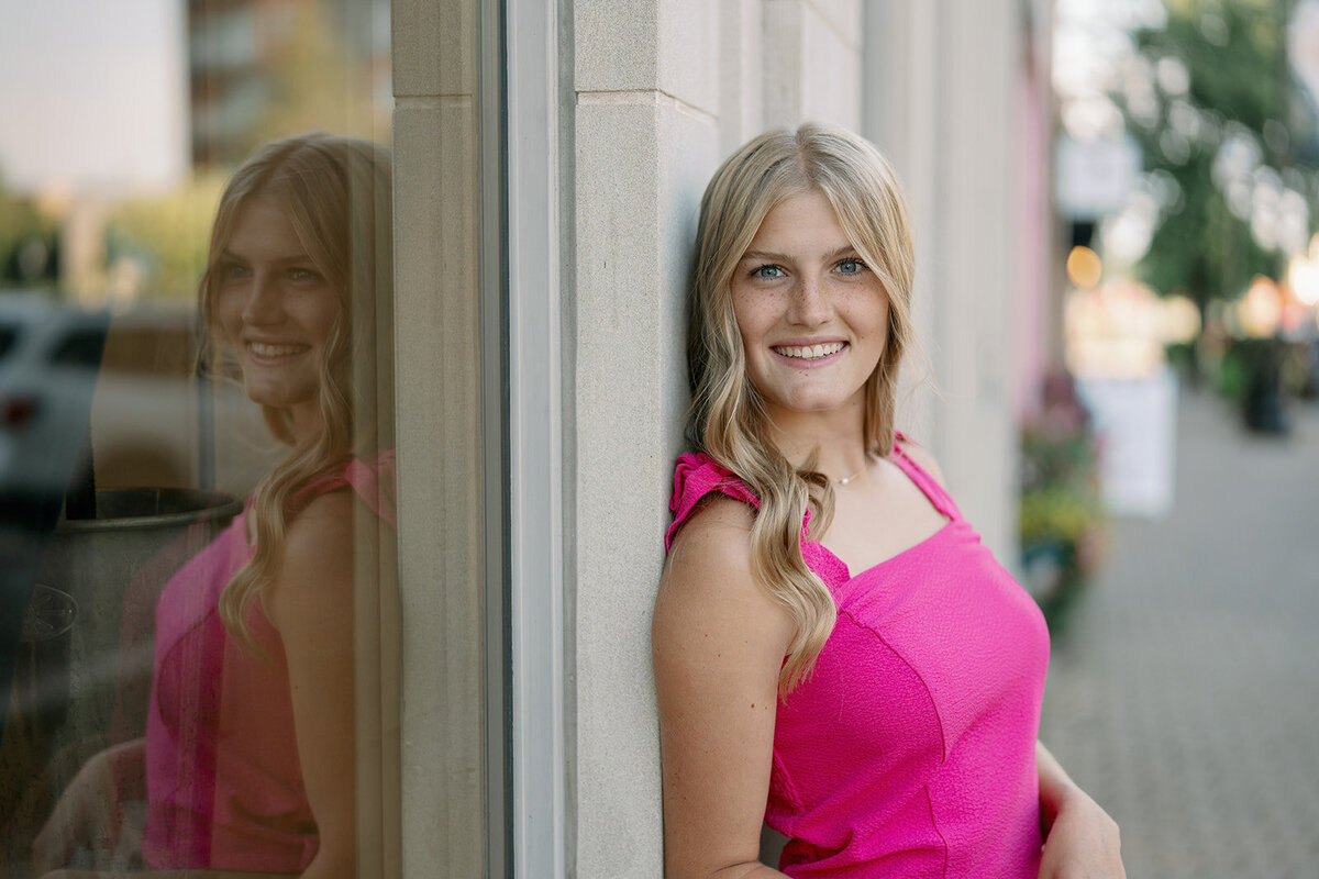 Close-up portrait of a senior girl smiling in a pink top during her downtown Holland senior photography session.